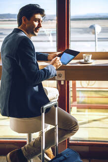 Geschäftsmann schaut weg, während er ein digitales Tablet im Flughafencafé hält - EHF00399