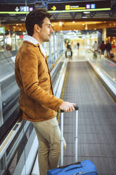 Nachdenklicher Geschäftsmann hält sein Gepäck auf dem Rollsteig eines Flughafens - EHF00400