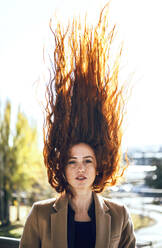 Selbstbewusste Frau mit fliegenden roten Haaren an einem sonnigen Tag - EHF00408