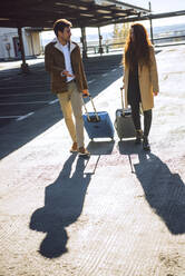 Business-Paar zieht Gepäck auf dem Flughafenparkplatz an einem sonnigen Tag - EHF00425