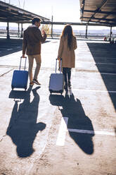 Business-Paar zieht Gepäck beim Gehen auf dem Flughafenparkplatz während des sonnigen Tages - EHF00427