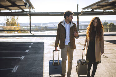 Business couple talking while pulling luggage at airport parking lot - EHF00429