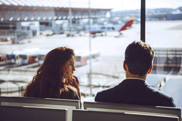 Business couple talking while sitting at airport departure area - EHF00441