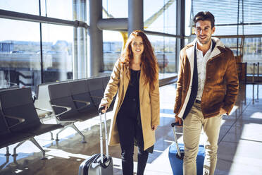 Confident business couple standing with luggage at airport departure area - EHF00444