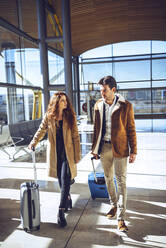 Business couple talking while walking with luggage at airport departure area - EHF00445