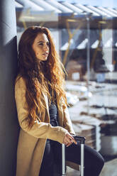 Thoughtful businesswoman standing with luggage by window at airport departure area - EHF00453