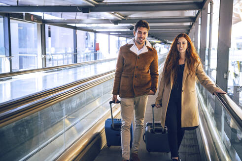 Business couple with luggage walking on moving walkway at airport - EHF00459