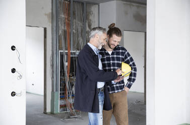 Architect and construction worker discussing over digital tablet while standing in renovating house - MJFKF00420