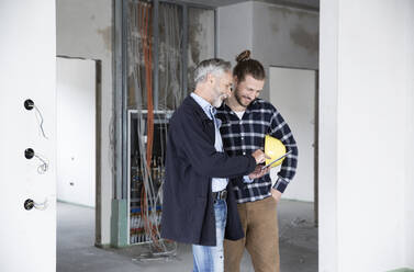 Architekt und Bauarbeiter diskutieren über ein digitales Tablet, während sie in einem zu renovierenden Haus stehen - MJFKF00420