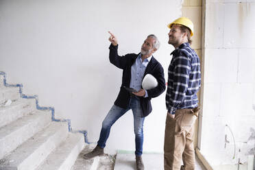 Männlicher Architekt, der einen Bauarbeiter anleitet, während er auf einer Treppe bei der Renovierung eines Hauses steht - MJFKF00421