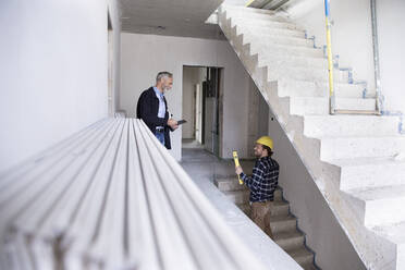 Architect and construction worker discussing while standing in constructing house - MJFKF00422