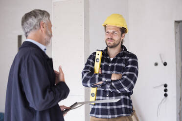 Architect and construction worker discussing while standing in constructing home - MJFKF00434