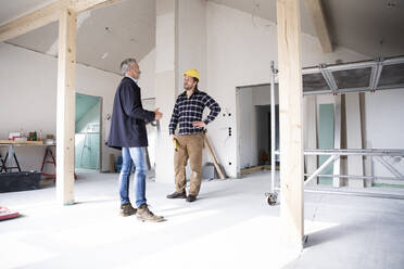 Architect and construction worker discussing while standing in renovating house - MJFKF00435