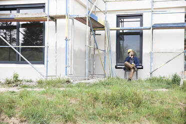 Bauarbeiter, der mit seinem Handy spricht, während er an einem Haus sitzt - MJFKF00450