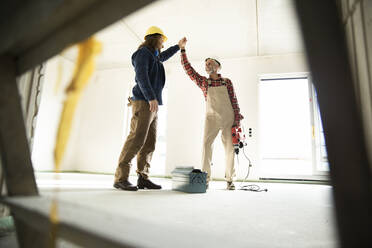 Male coworkers giving high five while standing in renovating house - MJFKF00466