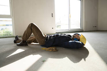 Bauarbeiter mit Händen hinter dem Kopf schlafend auf dem Boden in einem im Bau befindlichen Haus - MJFKF00470