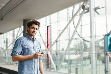 Confident casual businessman using smart phone while standing ta railroad station - SODF00820