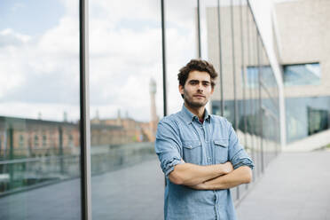 Handsome casual businessman with arms crossed standing against modern building - SODF00822