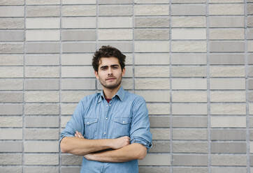 Handsome casual businessman with arms crossed standing against brick wall - SODF00825