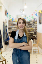 Smiling young woman with arms crossed standing in studio - EGAF00396