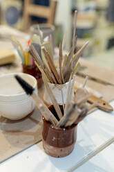 Close-up of brushes in desk organizers on workbench in studio - EGAF00406