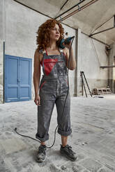 Thoughtful female stonemason holding radial saw looking away while standing in workshop - VEGF02434