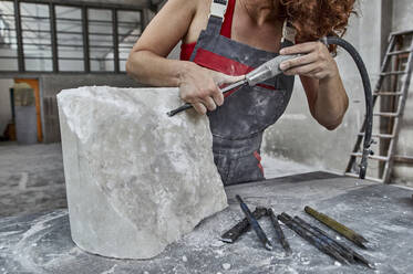 Steinmetz bearbeitet Stein mit Presslufthammer auf Tisch in Werkstatt - VEGF02444
