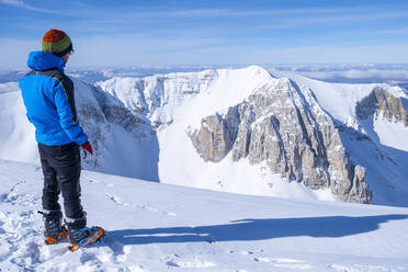 Junger Mann, der auf einem schneebedeckten Berg stehend die Aussicht betrachtet, Umbrien, Italien - LOMF01184