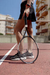Eine Tennisspielerin hält einen Schläger, während sie an einem sonnigen Tag auf einem Sportplatz steht - EGAF00409