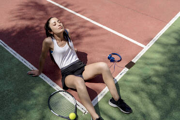 Tennisspielerin mit geschlossenen Augen, die sich auf dem Boden eines Sportplatzes entspannt - EGAF00418