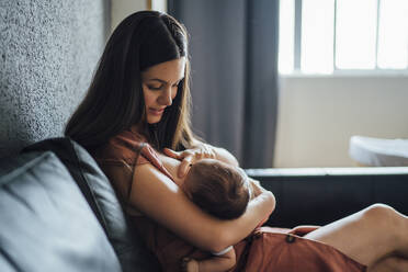 Mother breastfeeding baby boy while sitting on sofa at home - OCMF01425