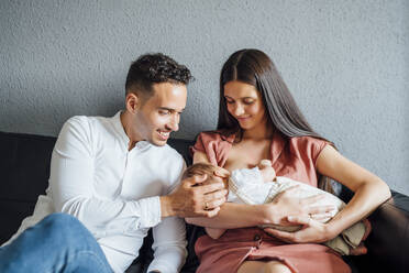 Happy father looking at baby boy being breastfed by mother at home - OCMF01441