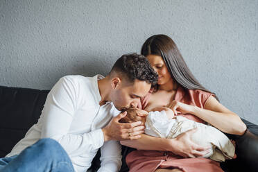 Happy father kissing baby boy being breastfed by mother at home - OCMF01442