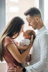 Happy parents playing with baby boy by window at home - OCMF01445