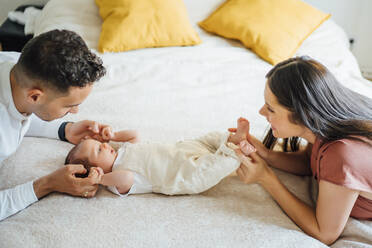 Happy parents holding baby boy on bed at home - OCMF01449