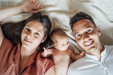 Smiling parents lying with baby boy on bed at home - OCMF01460