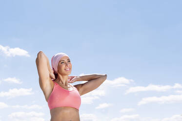 Sporty woman wearing headscarf while standing against blue sky - JCMF00944