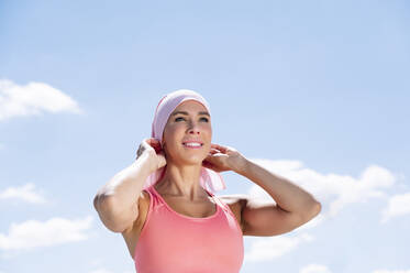 Thoughtful sporty woman wearing headscarf while standing against blue sky - JCMF00945