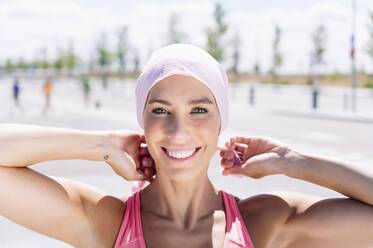 Happy sporty woman tying headscarf on street - JCMF00946