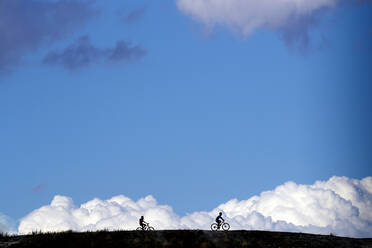 Silhouette Radfahrer fahren Fahrräder auf Feld gegen bewölkten blauen Himmel - OCMF01465