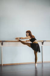 Happy ballet dancer stretching leg in dance studio - DAWF01728