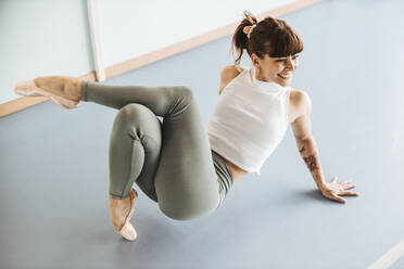 Happy ballet dancer exercising on floor in dance studio - DAWF01732