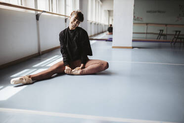 Glückliche Balletttänzerin streckt die Beine auf dem Boden im Studio - DAWF01741