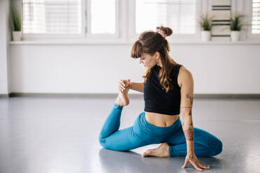 Female ballerina doing stretching exercises on floor in studio - DAWF01755