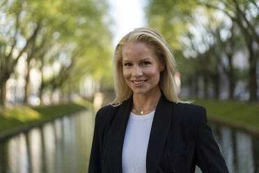 Lächelnd schöne blonde Unternehmerin stehend gegen Kanal in der Stadt - JOSEF00950