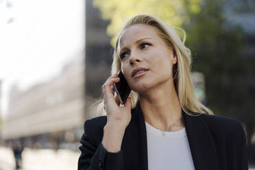 Blonde Geschäftsfrau schaut weg, während sie in der Stadt mit dem Handy telefoniert - JOSEF00962