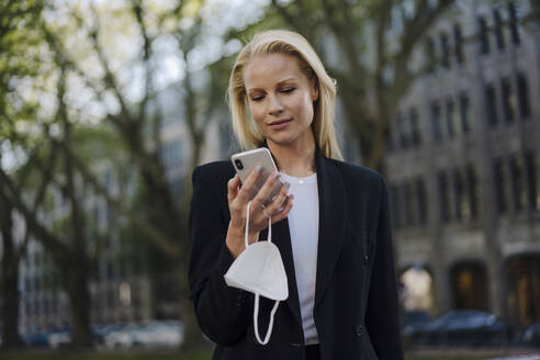 Beautiful businesswoman using mobile phone while standing in city - JOSEF00967