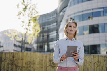 Beautiful female entrepreneur looking away while holding digital tablet at financial district in city - JOSEF01019