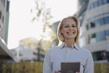 Glückliche blonde Geschäftsfrau mit digitalem Tablet im Finanzviertel der Stadt - JOSEF01021