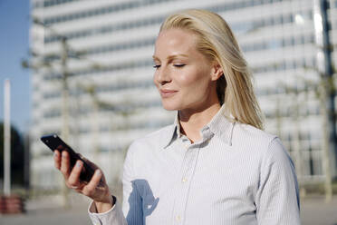 Blonde business woman checking smartphone on city rooftop stock photo